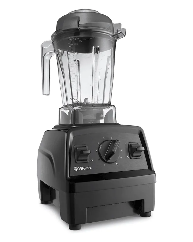 A blender container with fruit and a tamper tool on a kitchen counter.