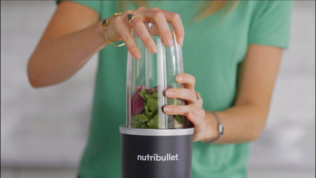 Bullet blender on a kitchen counter beside a green smoothie and fresh fruit