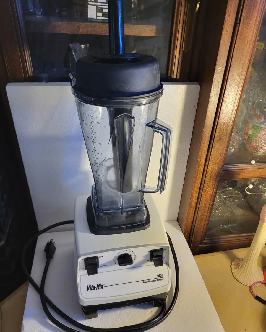 A chef's knife and diced vegetables on a cutting board beside a kitchen blender.