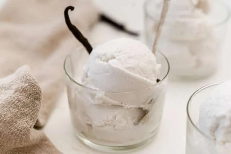 Copper scoop lifting creamy vanilla ice cream from metal bowl