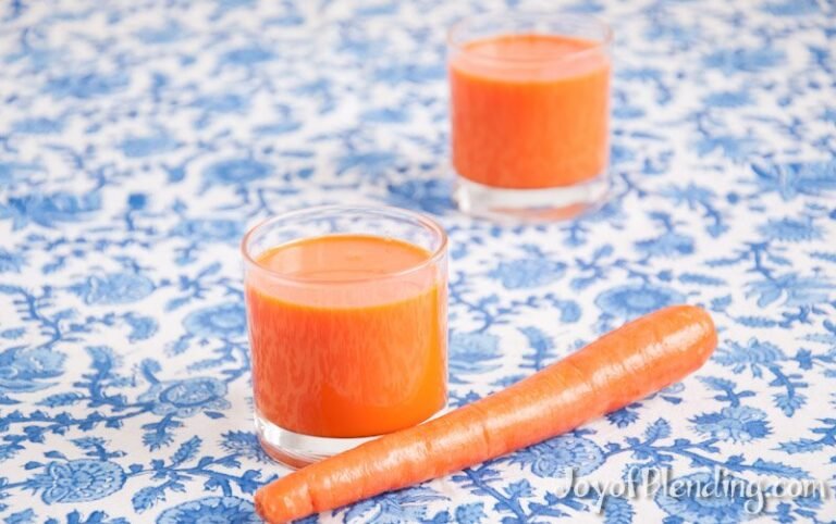 Fresh carrot juice in a glass beside a blender and raw carrots