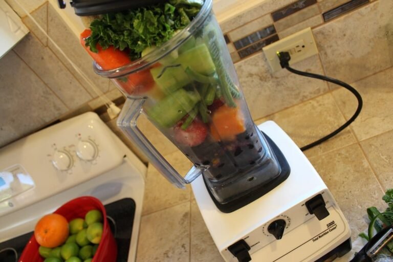 Fresh fruits and vegetables arranged around a Vitamix blender on a modern kitchen counter.