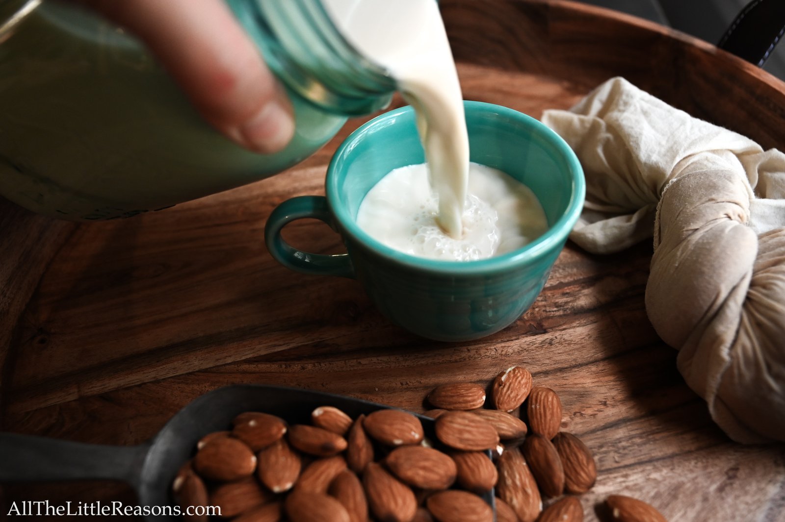 Fresh homemade almond milk in a blender surrounded by raw almonds on a kitchen counter