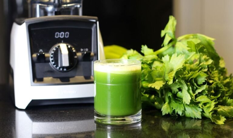 A glass of fresh celery juice next to a blender on a kitchen counter.