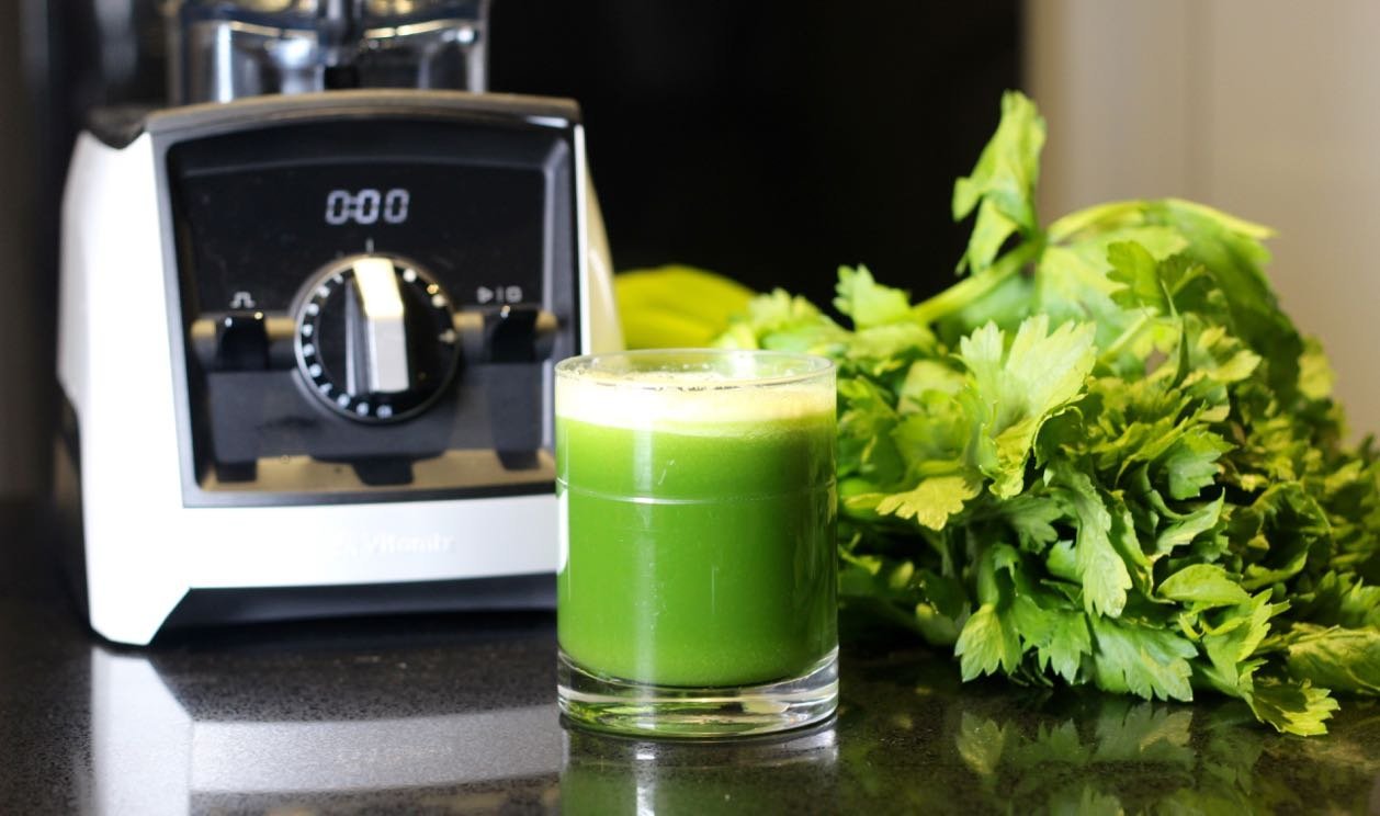 A glass of fresh celery juice next to a blender on a kitchen counter.
