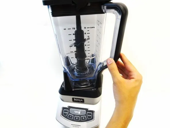 Hands carefully unlocking a Ninja blender pitcher from its base in a kitchen.