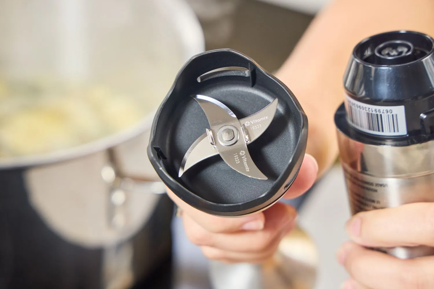 Hands preparing to use an immersion blender for blending fresh herbs in a bowl.