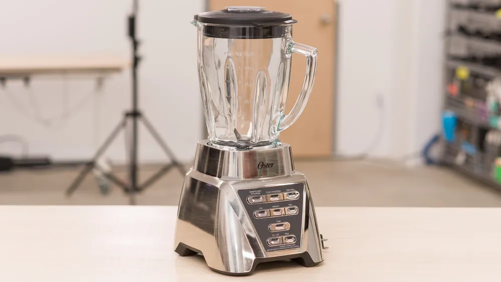Hands pressing the power button on an Oster countertop blender