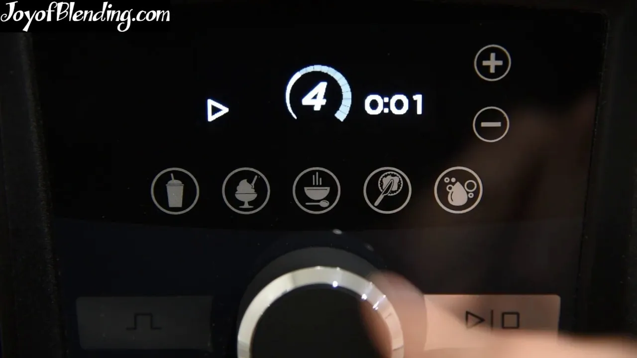 Hands pressing the power button on a Vitamix blender control panel in natural light.