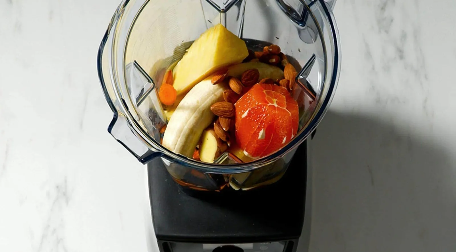 Hands securing a Vitamix pitcher and selecting the Smoothie preset button on a modern kitchen counter