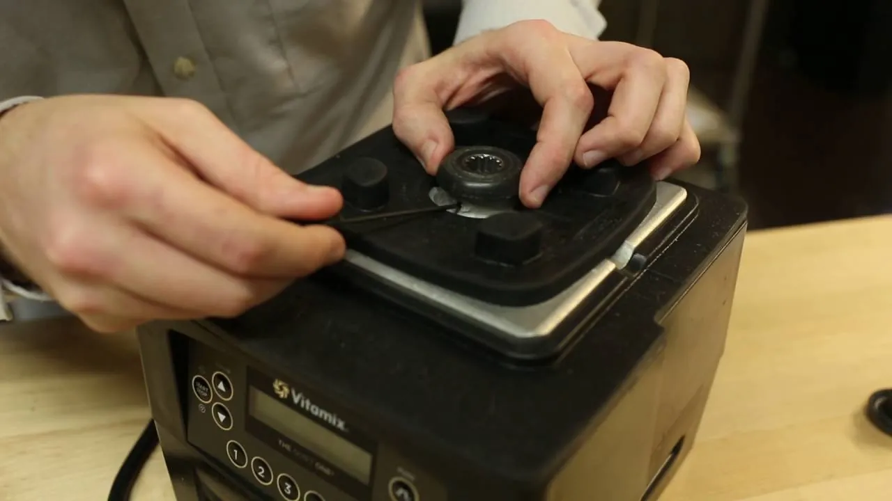 Hands using a blade removal tool to unlock the nut on a blender container.