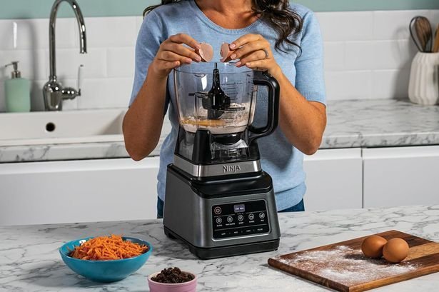 A modern Ninja blender sits on a clean kitchen counter with fresh produce.