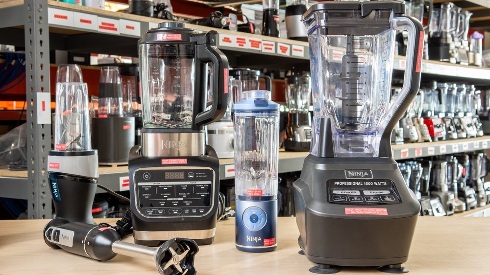 A modern Ninja blender sits on a kitchen counter surrounded by fresh fruit and vegetables.