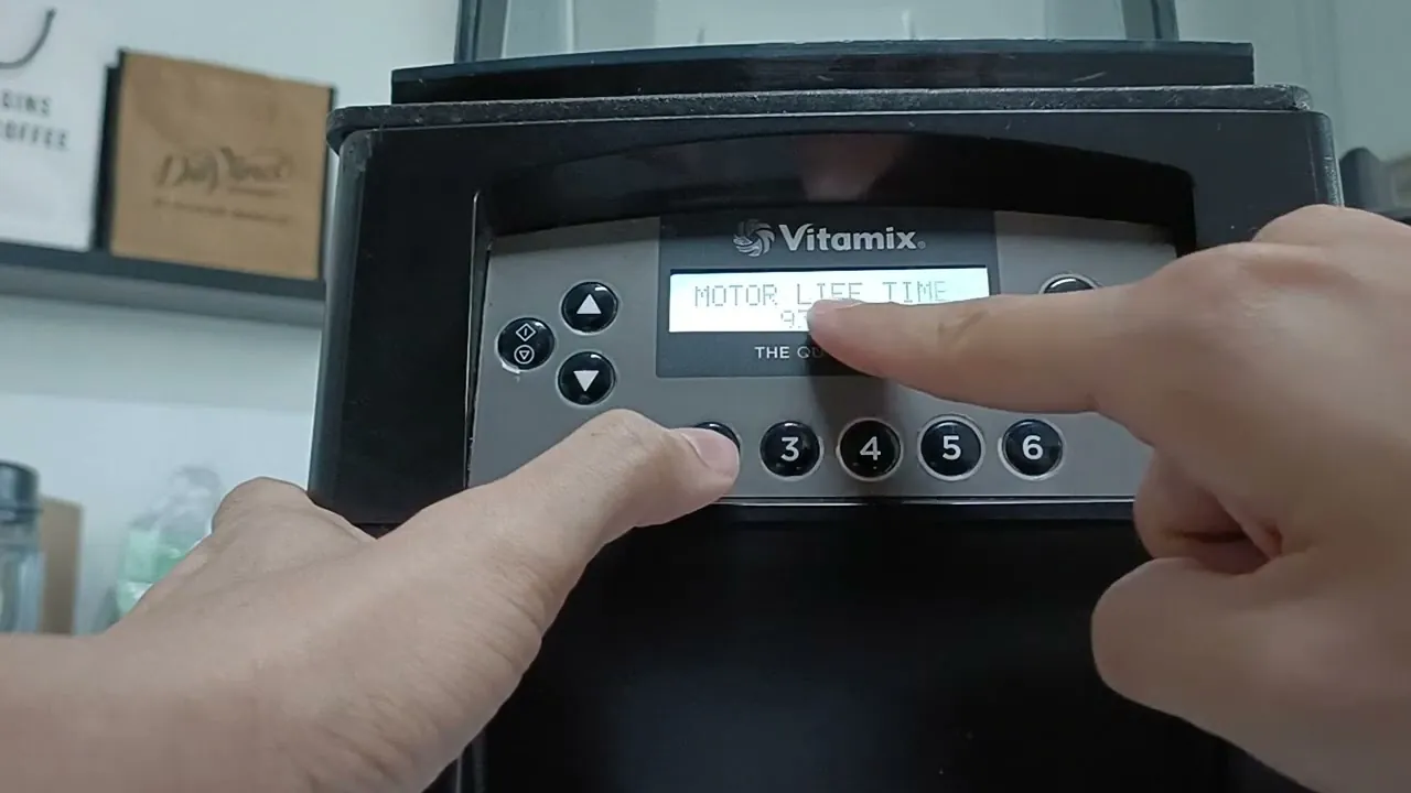 Person's hands pressing the power button on a Vitamix blender base on a clean countertop.