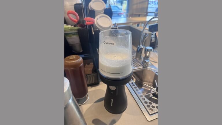 A professional cold foam blender sits on a modern marble countertop in a cafe.
