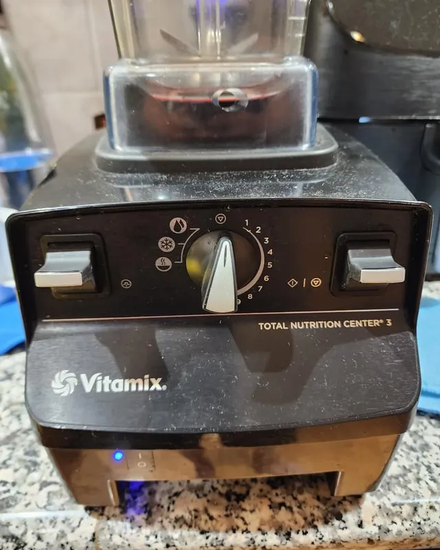 Unplugged Vitamix blender base on ceramic tile with coiled power cord beside it.