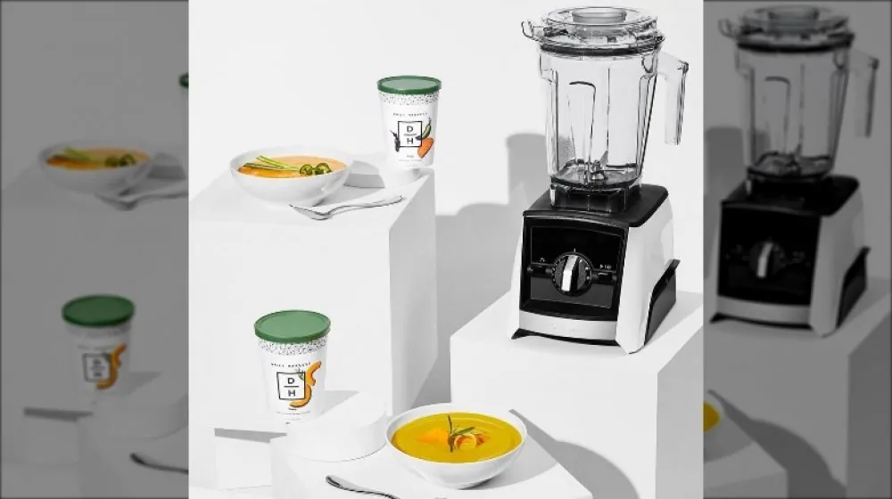 A variety of blender containers and a tamper are arranged on a kitchen island.