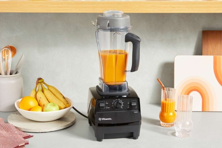 Vitamix blender blending a vibrant green smoothie on a marble countertop in natural light