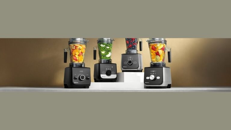 Vitamix blender container on a light oak counter with a smooth green smoothie inside