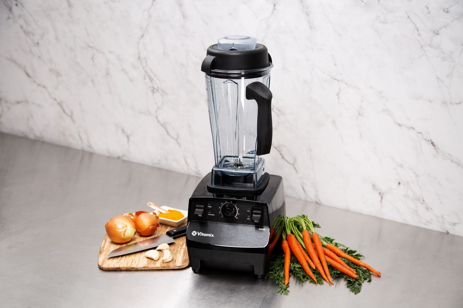 Vitamix blender with fresh ingredients and poured smoothie on a marble countertop